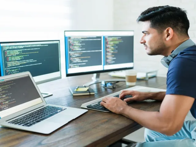 Desenvolvedor em escritório com 3 monitores escrevendo códigos para desenvolver software com 3 monitores