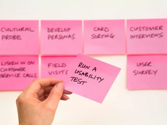 Papéis rosas colados na parte com uma mão segurando um deles com a seguinte frase: Execute o teste de usabilidade