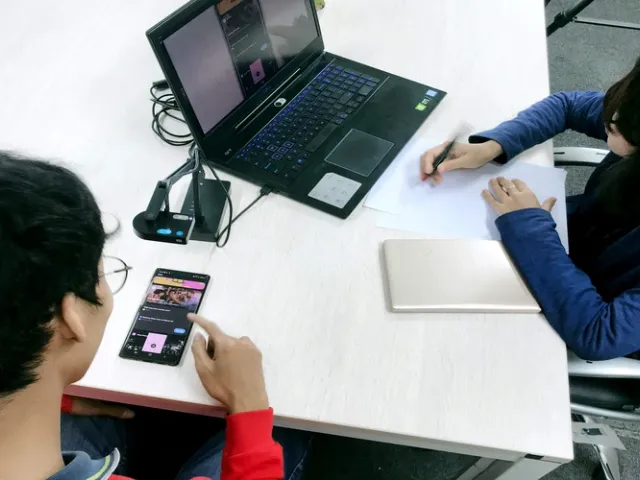 2 profissionais de TI fazendo teste de usabilidade de software em escritório com mesa branca, com um celular e um notebook sendo usado por eles