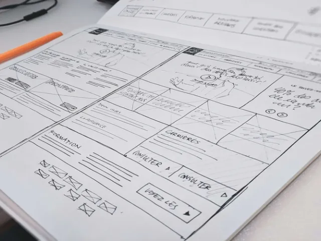 Bancada com um papel com planejamento e anotações de desenvolvimento de software, com uma caneta de cor laranja na esquerda da mesa.